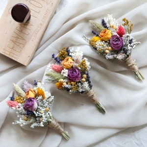 Dried flower boutonniere set with purple, orange, and yellow blooms and sage-green accents