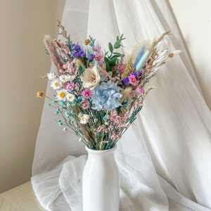 Colorful preserved flowers bouquet with dried stems in a white vase
