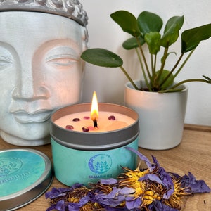 Teal tin soy wax candle with lotus emblem, burning flame, pink wax surface with flower petals
