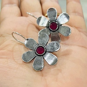 Silver flower stud earrings with red centers and five textured petals