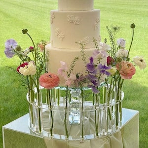 Floral cake stand with clear glass vases and pastel flowers around a white tiered cake