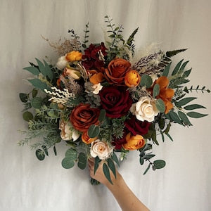 Bridal bouquet with burgundy, rust orange and cream flowers, greenery, held by hand
