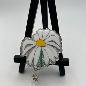 White daisy flower badge reel with yellow center and silver frame, black clasp