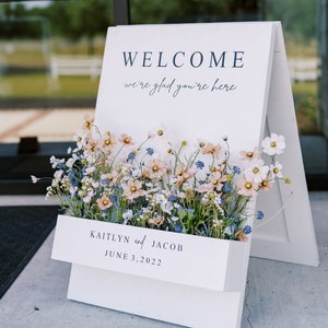 Welcome sign with floral border on tabletop easel, includes date and names