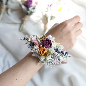 Dried flower wrist corsage with purple and orange blooms on a fabric wrist band