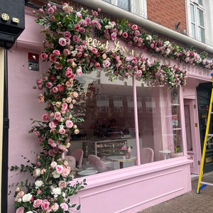 Pink and white flower garland with green leaves and wreaths framing a storefront window