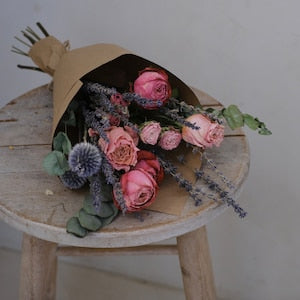 Dried rose bouquet bundle in kraft wrap with pink roses, purple blooms, and green foliage.