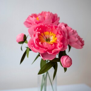 Pink crepe paper peony flower with buds and green leaves in a vase
