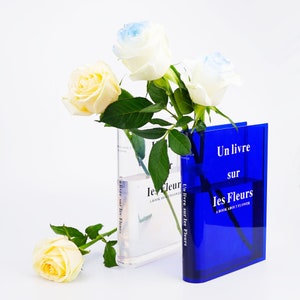 Clear acrylic book vase holding white and yellow flowers, rectangular blue cover