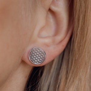 Silver round stud earrings with flower-of-life pattern detail on earlobe