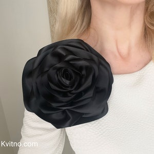 Large black fabric rose flower brooch on a white top