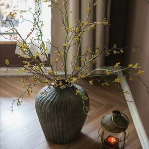 Long Weigela flower stem in dark ribbed vase with thin branches and small blossoms
