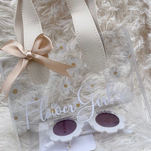 White floral flower-girl gift bag with satin bow and two purple sunglasses