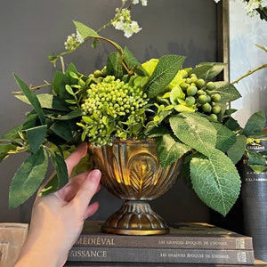 Green faux floral centerpiece in gold iron vase with lush greenery and berry-like blooms