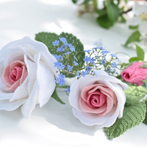 Handmade crochet rose flowers with pink centers, white petals, blue blooms and green leaves