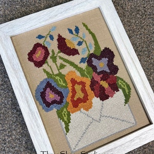 Counted cross stitch pattern featuring a multicolor floral motif in a light wood frame