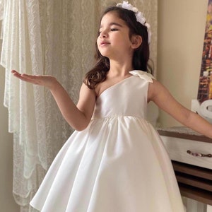 White satin one-shoulder dress with large bow at shoulder, knee-length skirt