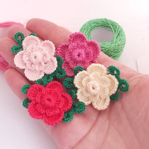 Crochet flower applique motifs with layered petals and green leaf accents, multicolor