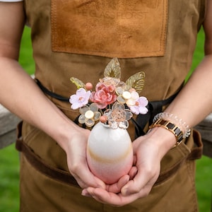 Glass flower bouquet vase with pink and white blossoms, held in hands