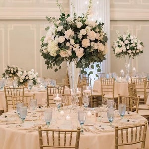 Artificial floral centerpiece with white roses and green leaves on a tall stand