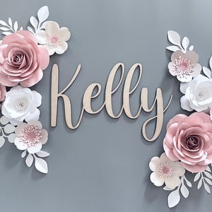 Light pink paper flower wall decor with script name 'Kelly' in gray