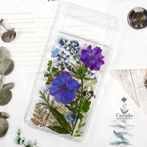 Clear pressed flower phone case with purple and blue blossoms and green leaves