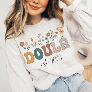 Heather gray crewneck sweatshirt with colorful floral "Doula est 2023" graphic