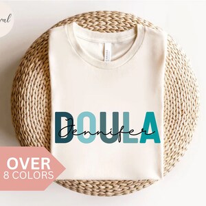 White crewneck t-shirt with teal "Doula" graphic