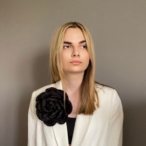 Large black rose brooch on a blazer lapel, round floral pin detail.