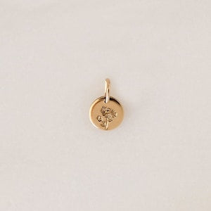 Gold-toned round charm pendant with delicate floral engraving and small cutout