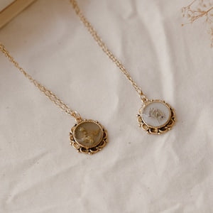 Gold-tone chain necklace with round pendant holding a pressed flower