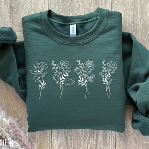 Green crewneck sweatshirt with white birth-month flower line-art graphic