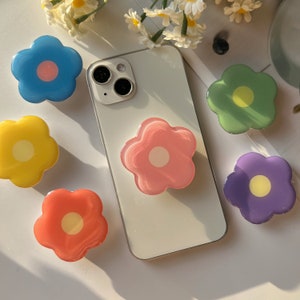 Flower-shaped transparent folding phone grips with yellow centers, colorful set around a phone