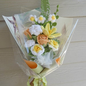 Handmade crochet flowers bouquet with white, yellow, and peach blooms wrapped in clear plastic