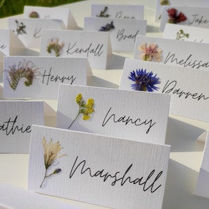Botanical pressed-flower place cards with handwritten names and small real flowers