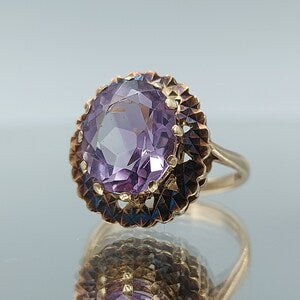 Gold-tone ring with large oval amethyst gemstone in ornate halo setting