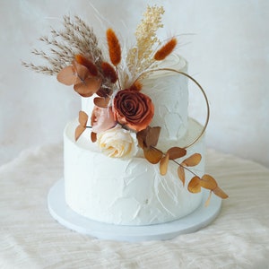 Dried autumn flower cake topper bouquet with orange-brown blooms on a white cake