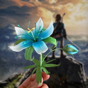 Blue and white flower replica with green leaves and stem, held in hand