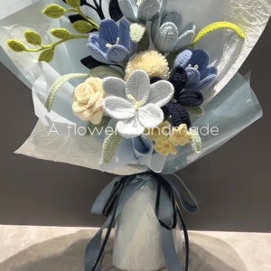 Handmade crochet flower bouquet with blue, white, and gray blossoms and yellow leaves, tied ribbon