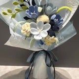 Handmade crochet flower bouquet with blue, white, and gray blossoms and yellow leaves, tied ribbon