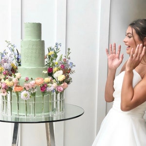 Glass round cake stand with a pastel floral crown and light green tiered cake