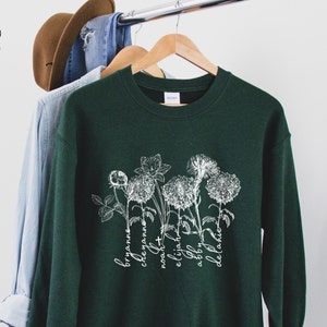 Dark green long-sleeve shirt with white floral birth-month graphic and cursive text