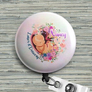 Round retractable badge reel with floral fetus design and name Nancy on lavender button