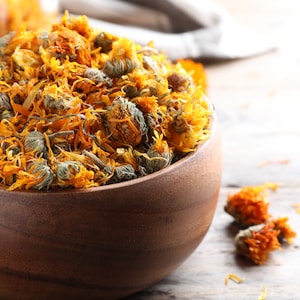 Dried whole calendula officinalis flowers in a wooden bowl