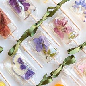Wildflower lollipop treats in clear wrappers with purple and pink pressed flowers, tied ribbon