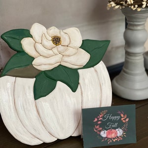 Wooden pumpkin bouquet with white magnolia flowers and green leaves on a stand, with greeting card