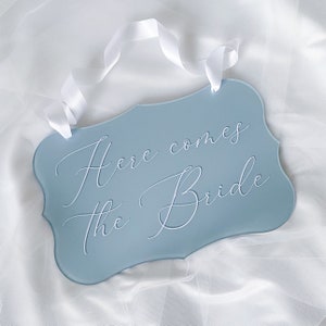 Light blue acrylic wedding sign with white cursive text: Here comes the Bride