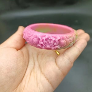 Pink jade bangle with carved peony flower detail around the band