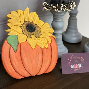 Wood pumpkin decor with orange carving and yellow sunflower bouquet, green leaf accents