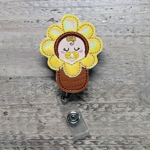 Flower-shaped baby girl badge with clip; yellow petals and brown stem